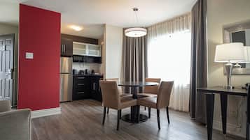Una habitación de hotel moderna con comedor, cocina y un ventanal con cortinas.