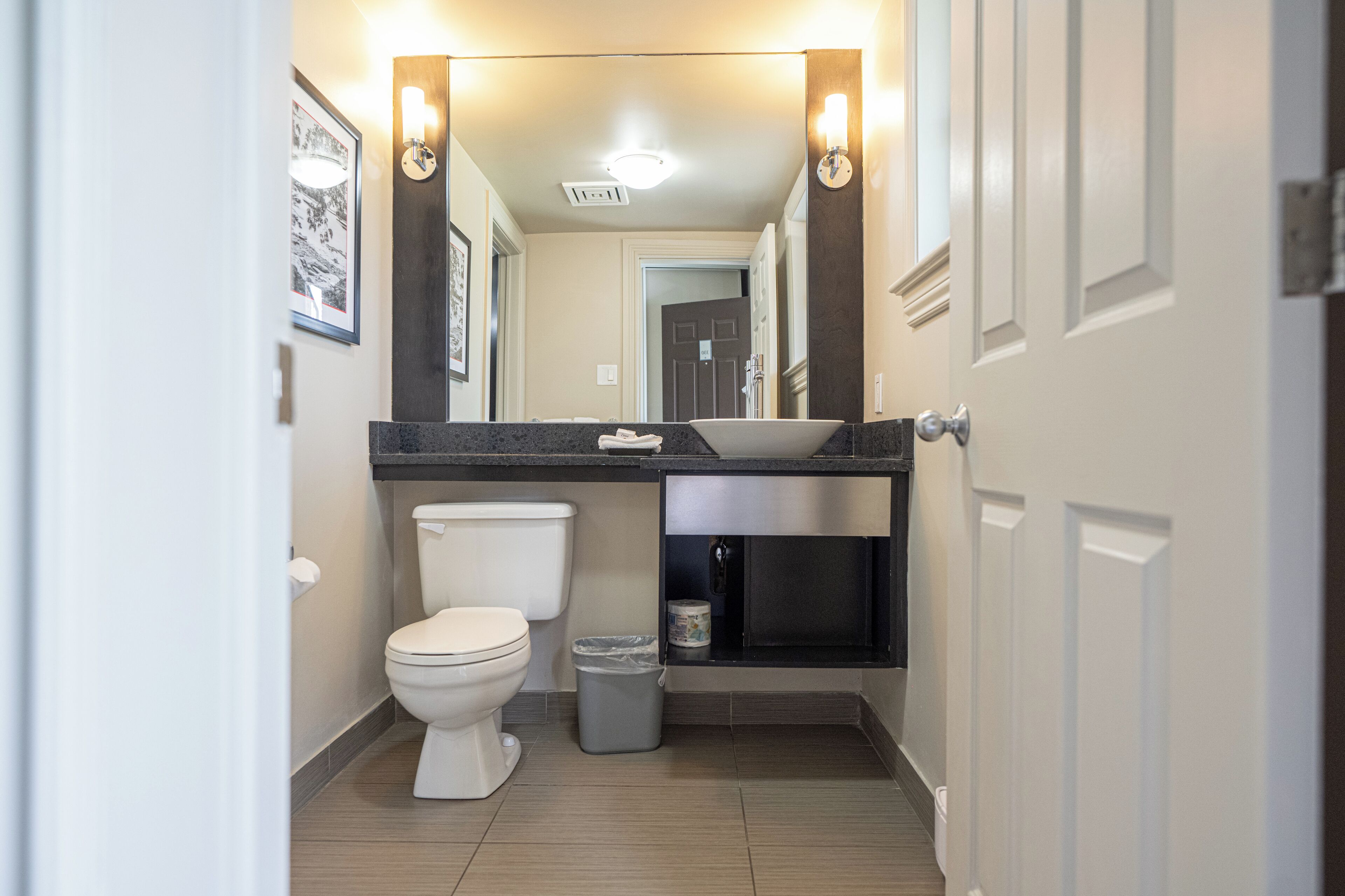 Un baño moderno con inodoro blanco, lavamanos con encimera oscura y un cubo de basura.