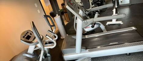 A gym with cardio machines, including treadmills and ellipticals, and a mirrored wall.