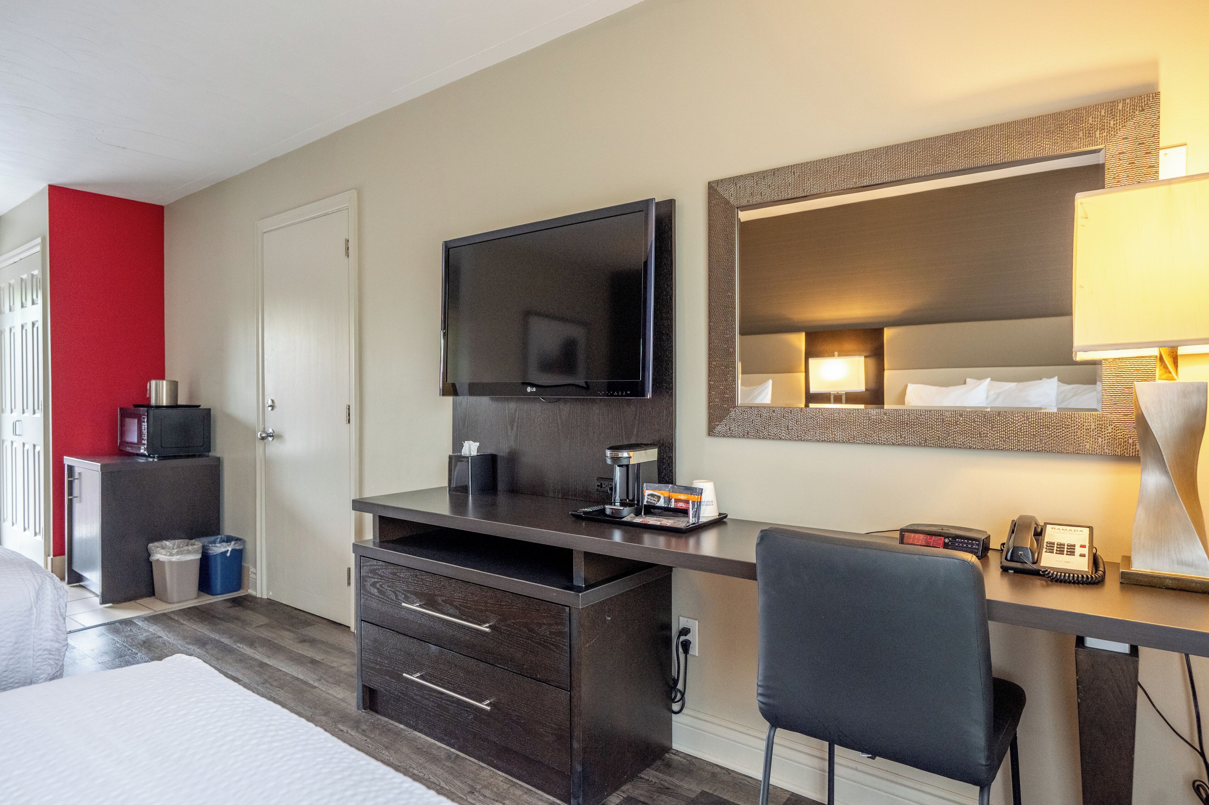 A hotel room with a bed, a desk with a TV, a mirror, a lamp, and a telephone.