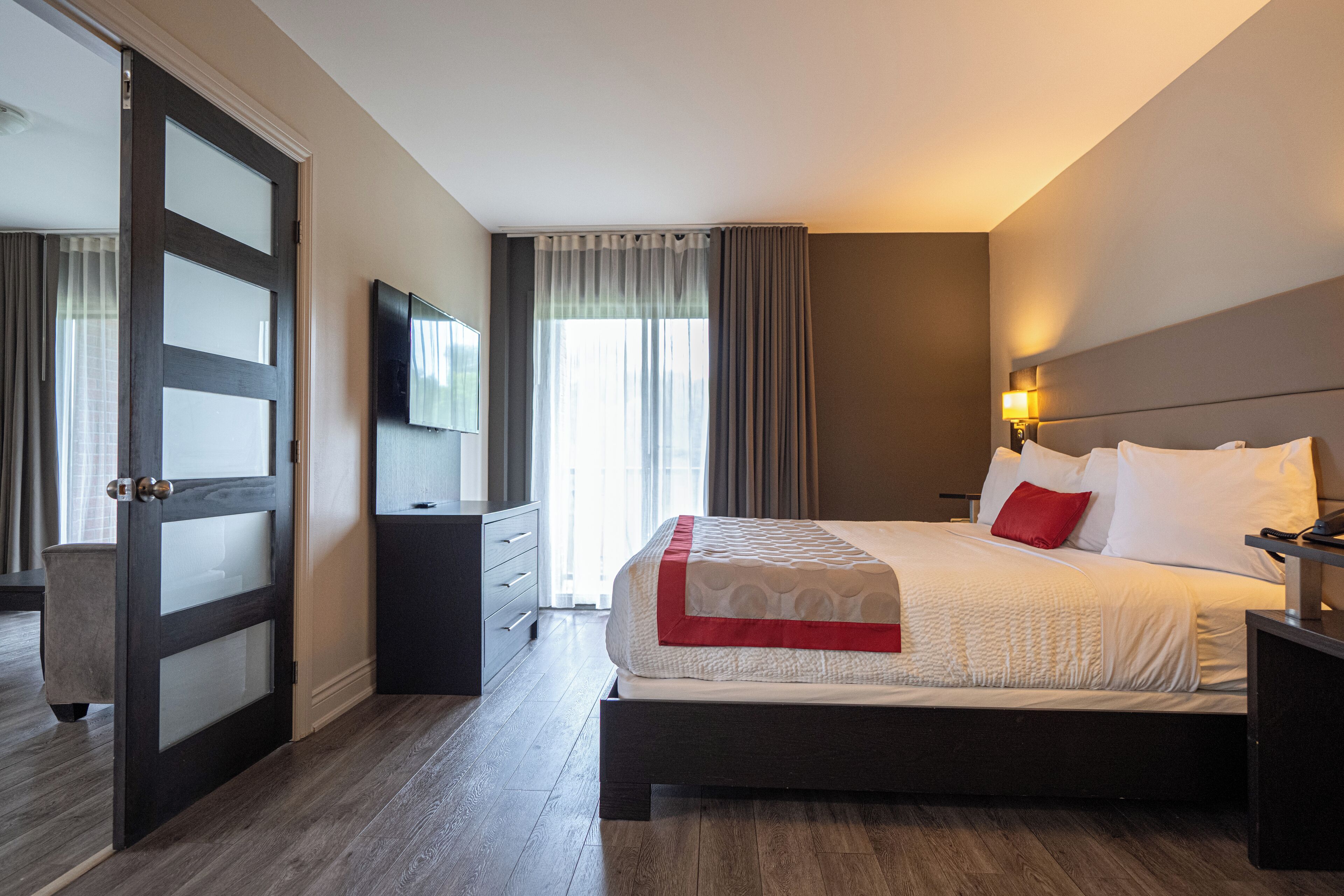A hotel room with a large bed, a TV mounted on the wall, a bedside table, and a door with frosted glass panels.