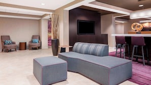 A modern hotel lobby with a sectional sofa, two armchairs, a small table, and a bar area with stools.