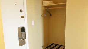 Une petite pièce étroite avec une porte blanche, une poignée en métal, un thermostat fixé au mur, une étagère avec des serviettes pliées et un étendoir métallique.