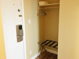 Una habitación pequeña y estrecha con una puerta blanca, un picaporte metálico, un termostato en la pared, una estantería con toallas dobladas y un tendedero de metal.