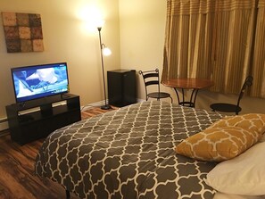 Une chambre à coucher avec un lit, une télévision, un lampadaire, une petite table et une chaise.
