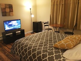 Un dormitorio con cama, televisión, lámpara de pie, una mesita y una silla.