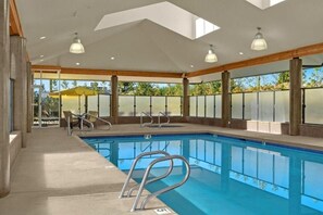 An indoor swimming pool with clear glass walls, a concrete deck, and a wooden ceiling.