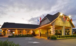 A hotel with a modern design, featuring a prominent entrance with flags, a well-lit facade, and a landscaped driveway.