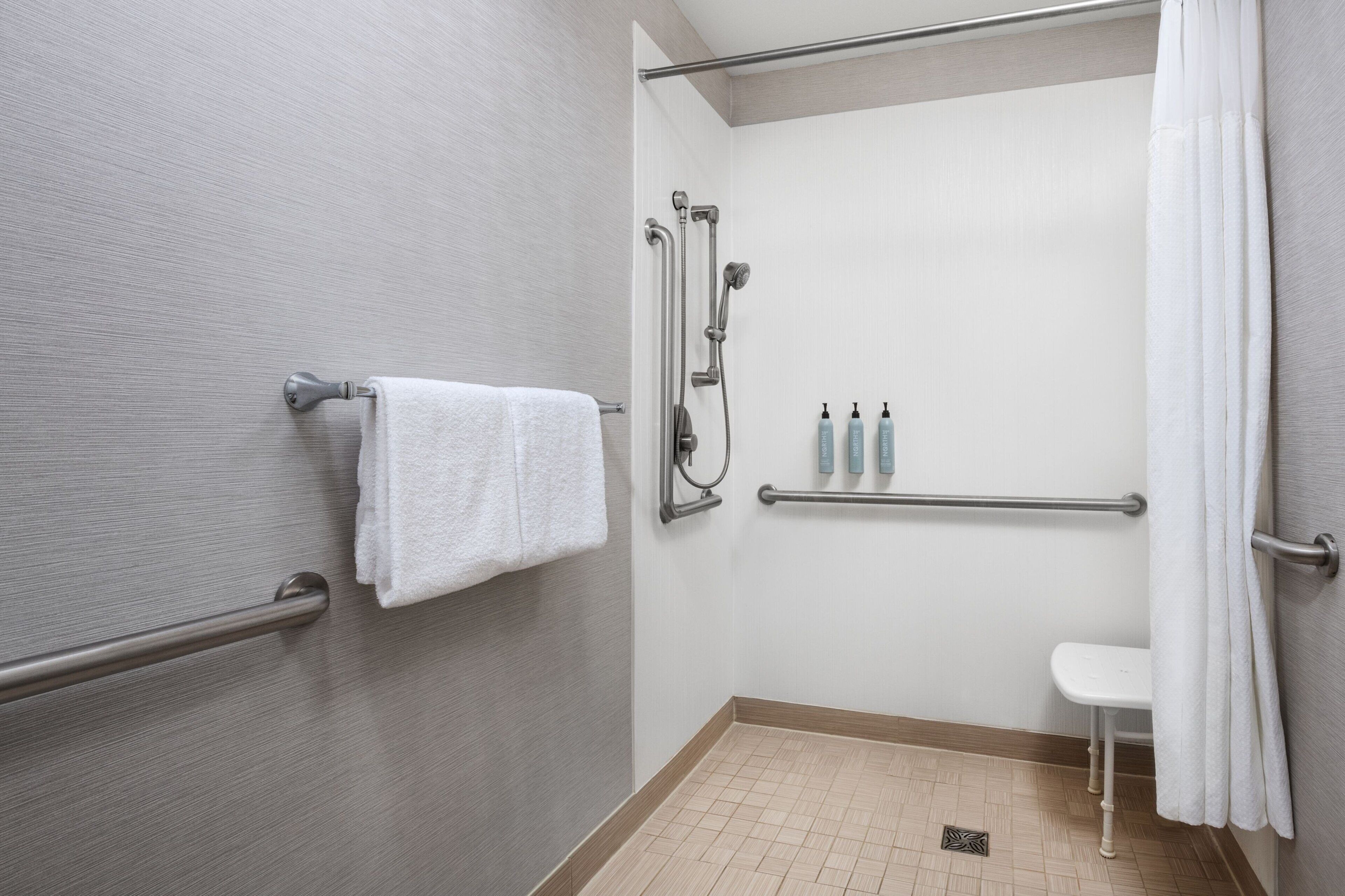 A modern bathroom with a walk-in shower, grab bars, a white towel, and toiletries on a shelf.