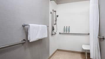 A modern bathroom with a walk-in shower, grab bars, a white towel, and toiletries on a shelf.