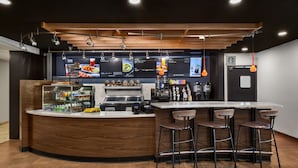 A modern bar area with a wooden counter, bar stools, and a menu display. - Courtyard by Marriott Anchorage Airport (Anchorage)