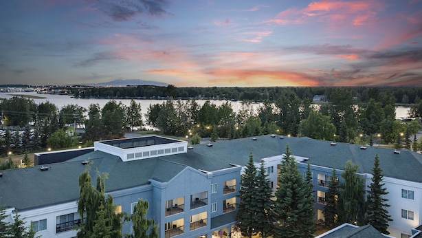A multi-story hotel with balconies, surrounded by trees and a view of a lake at sunset. - Courtyard by Marriott Anchorage Airport (Anchorage)