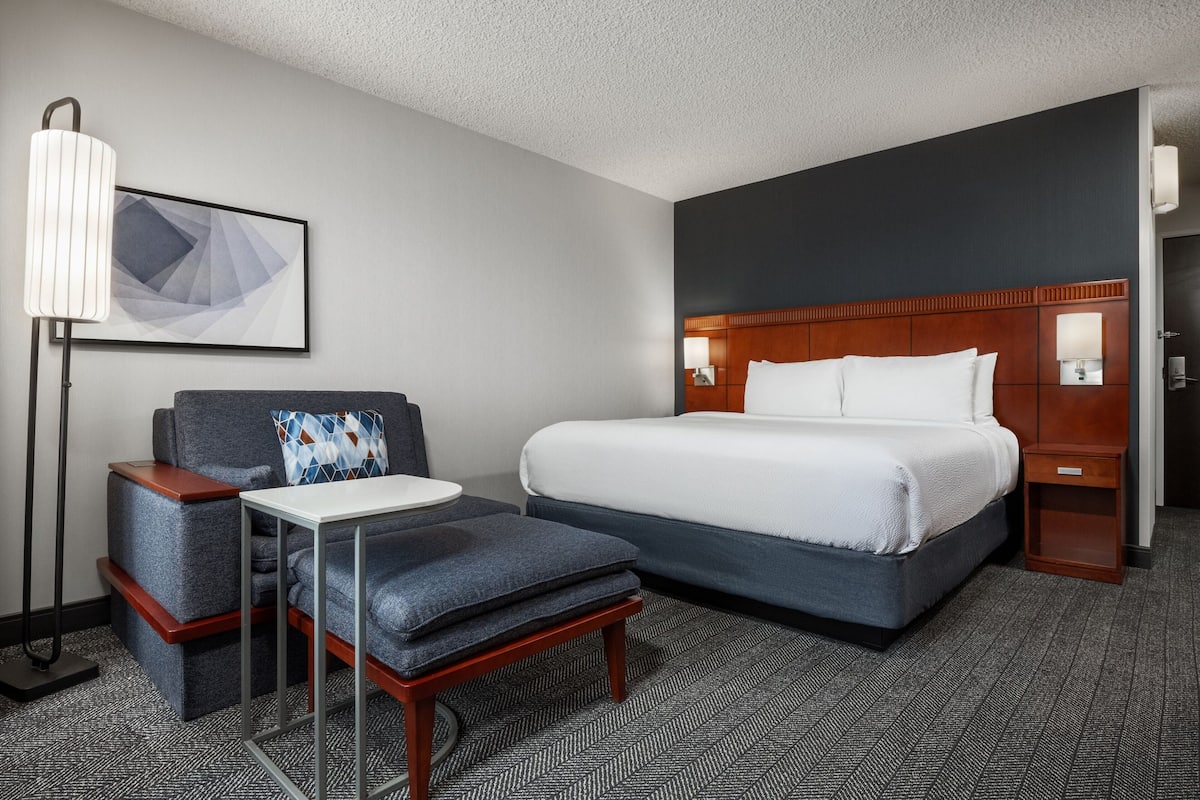 A hotel room with a large bed, a desk, a chair, and a floor lamp.