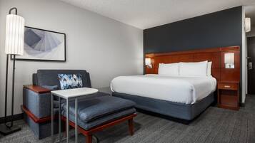 A hotel room with a large bed, a desk, a chair, and a floor lamp.