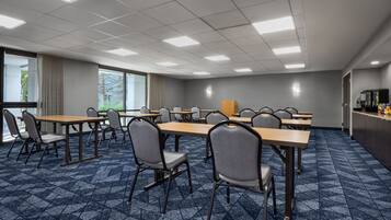A conference room with multiple tables and chairs, large windows, and a carpeted floor.