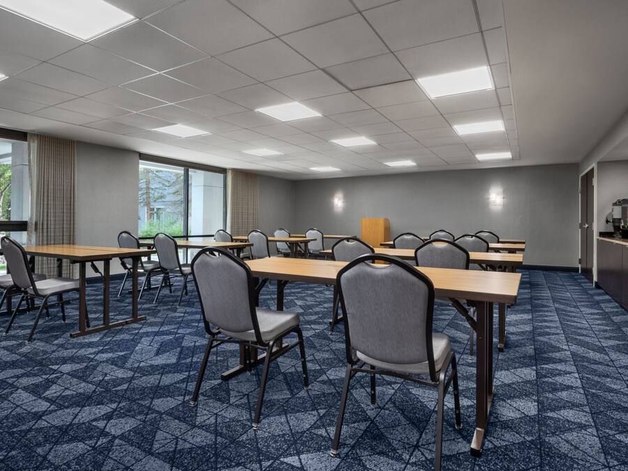 A conference room with multiple tables and chairs, large windows, and a carpeted floor.