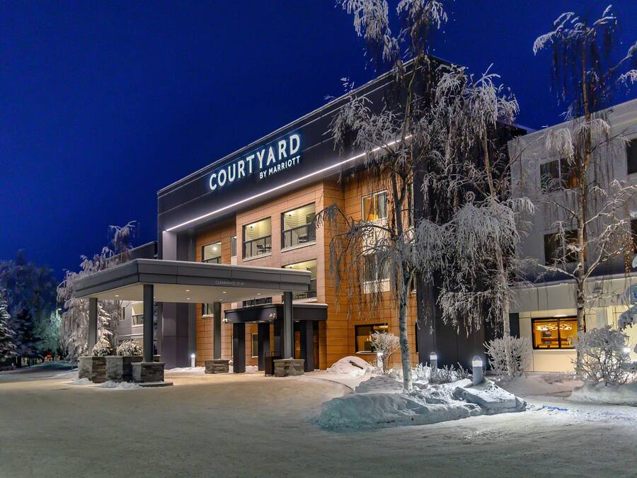 Un hôtel Courtyard by Marriott doté d’une entrée couverte, d’arbres couverts de neige et d’un ciel nocturne dégagé.