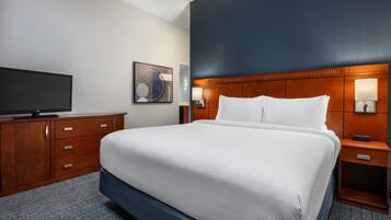 A hotel room with a large bed, wooden headboard, bedside lamps, a flat-screen TV, and a dresser.