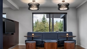 A modern living room with a dark blue sofa, two round wooden tables, and a flat-screen TV mounted on a dark wooden cabinet. - Courtyard by Marriott Anchorage Airport (Anchorage)