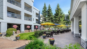 A courtyard with outdoor seating, potted plants, and a building with balconies. - Courtyard by Marriott Anchorage Airport (Anchorage)