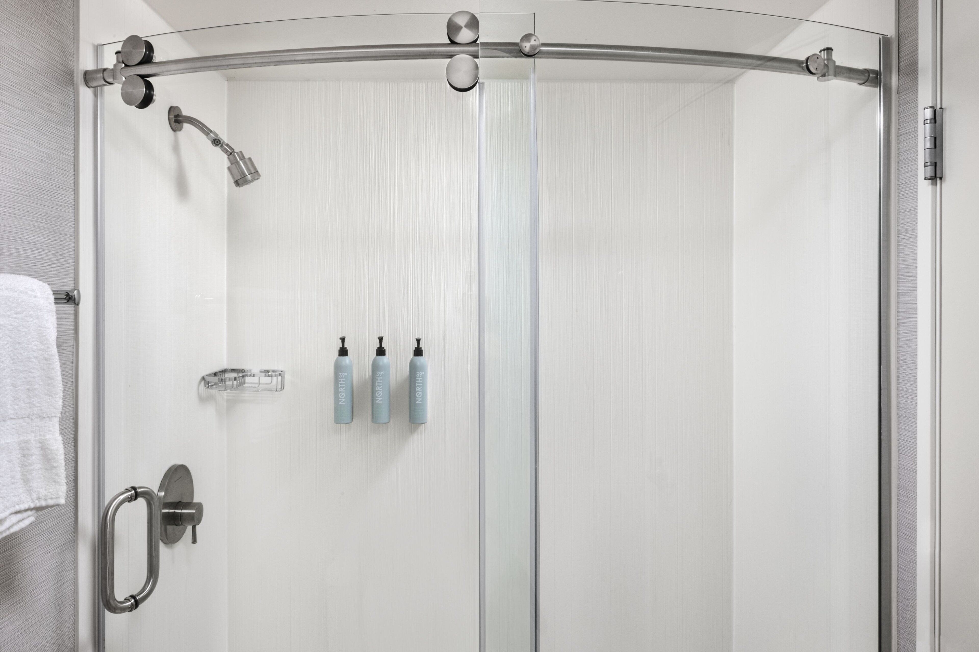 Una doccia con pareti in vetro e porta a forma di arco, un porta asciugamani e tre flaconi di shampoo.