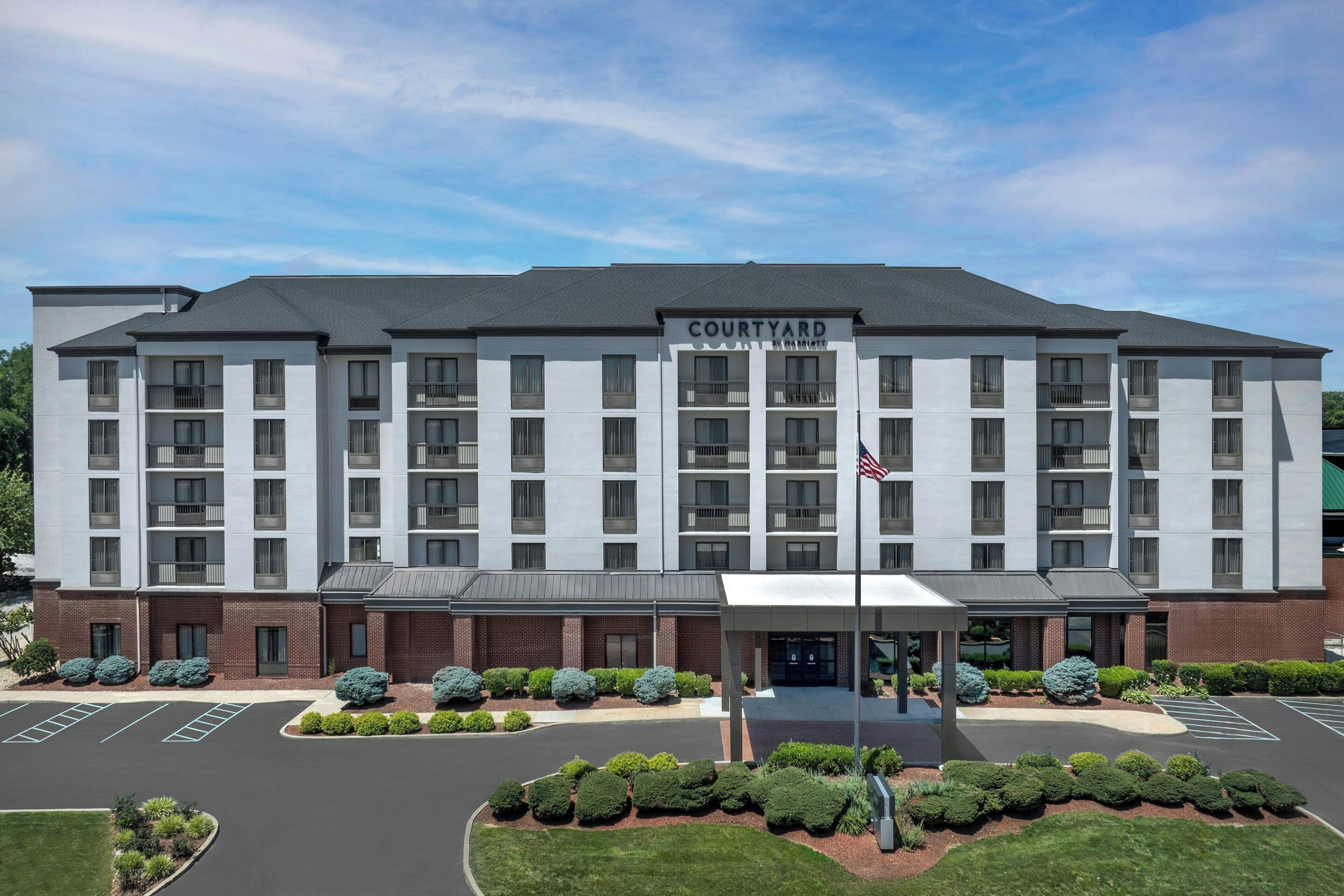 A multi-story hotel with a flat roof, a central entrance, and a parking lot.