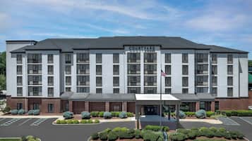 A multi-story hotel with a flat roof, a central entrance, and a parking lot.