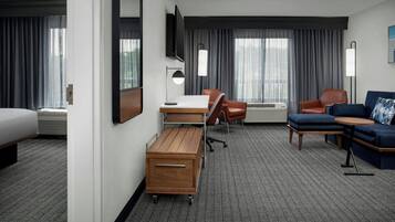 A hotel room with a bed, desk, chair, sofa, and a flat-screen TV.