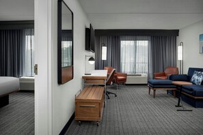 A hotel room with a bed, desk, chair, sofa, and a flat-screen TV. - Courtyard by Marriott Bloomington (Bloomington)