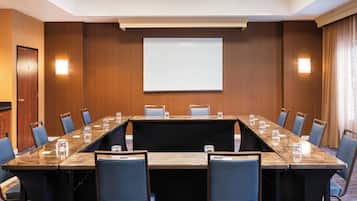 Un salón de conferencias con una larga mesa, sillas, una pantalla de proyector y un panel de pared de madera.