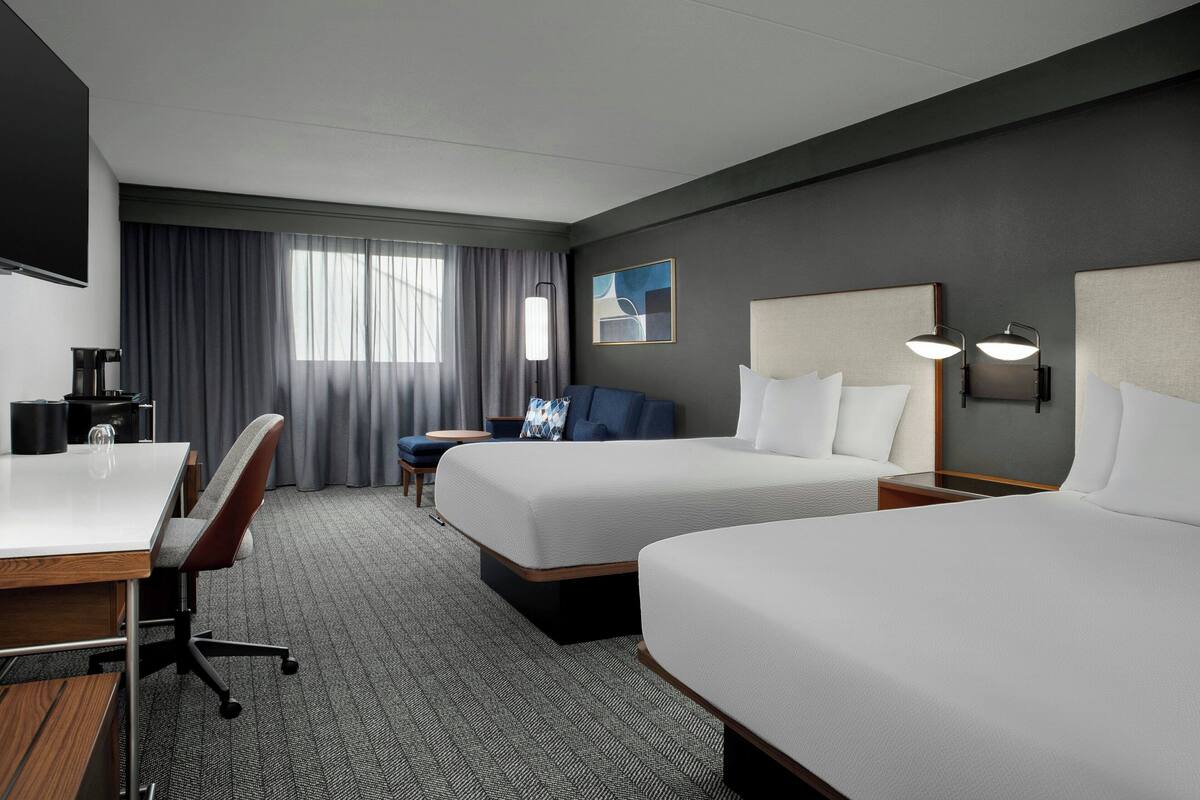 Une chambre d’hôtel avec deux lits, un bureau, une chaise, une machine à café et un téléviseur.