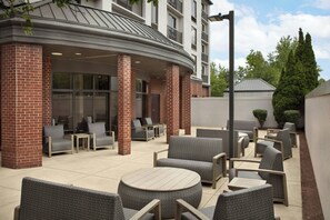 An outdoor seating area with wicker furniture and a covered section with glass doors. - Courtyard by Marriott Bloomington (Bloomington)