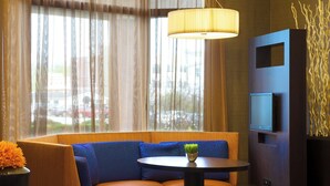 Una habitación de hotel moderna con zona de estar, una mesa, un televisor y un ventanal con cortinas.