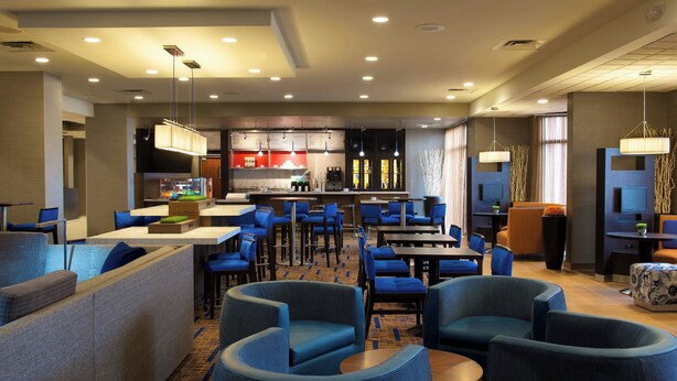 Un moderno vestíbulo de hotel con asientos azules, una zona de cocina y una pantalla de televisión.
