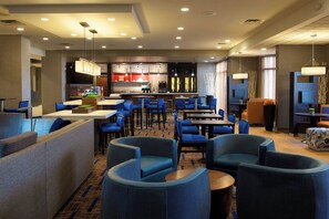 Un moderno vestíbulo de hotel con asientos azules, una zona de cocina y una pantalla de televisión.