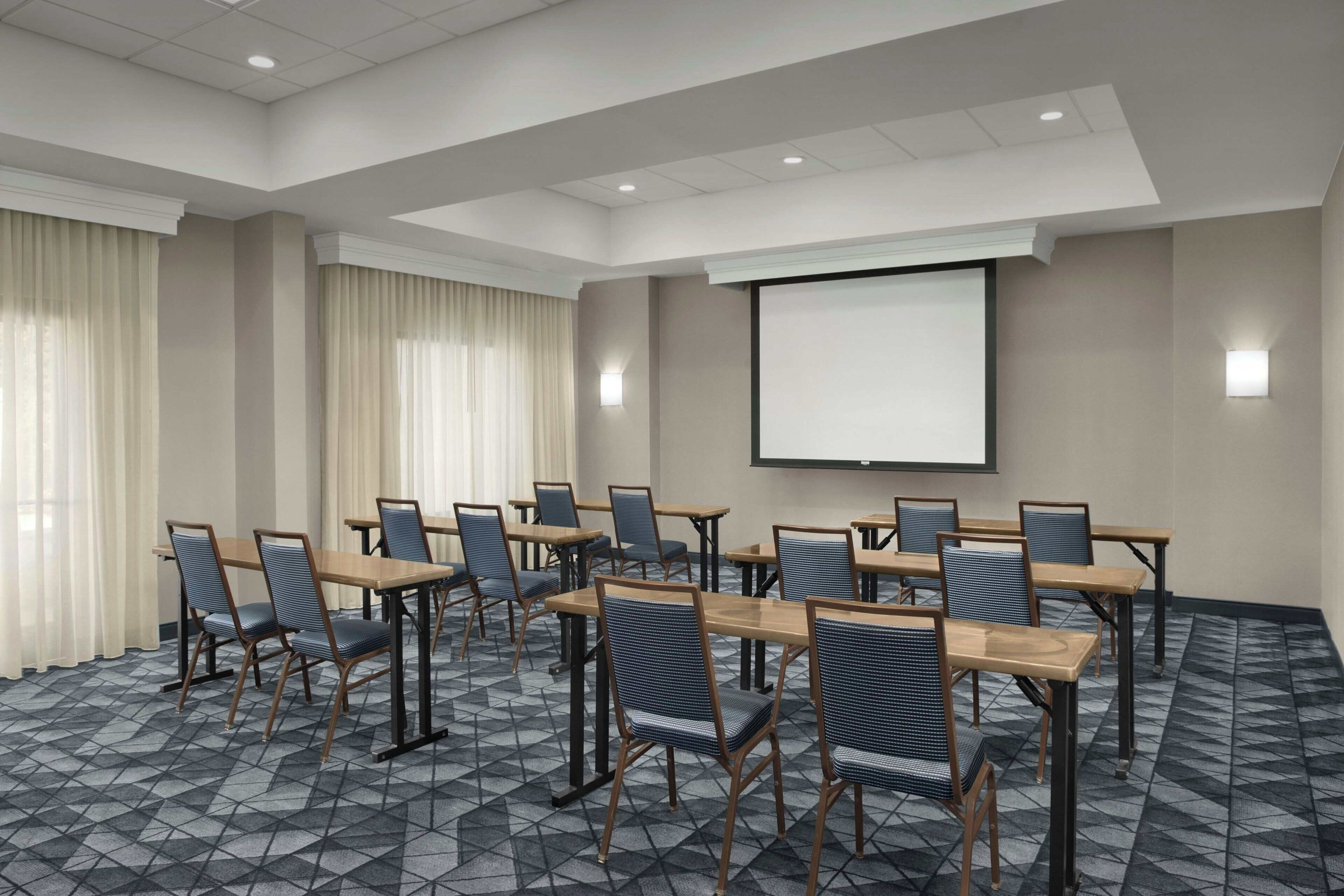 Een congreszaal met een projectiescherm, meerdere tafels en stoelen.