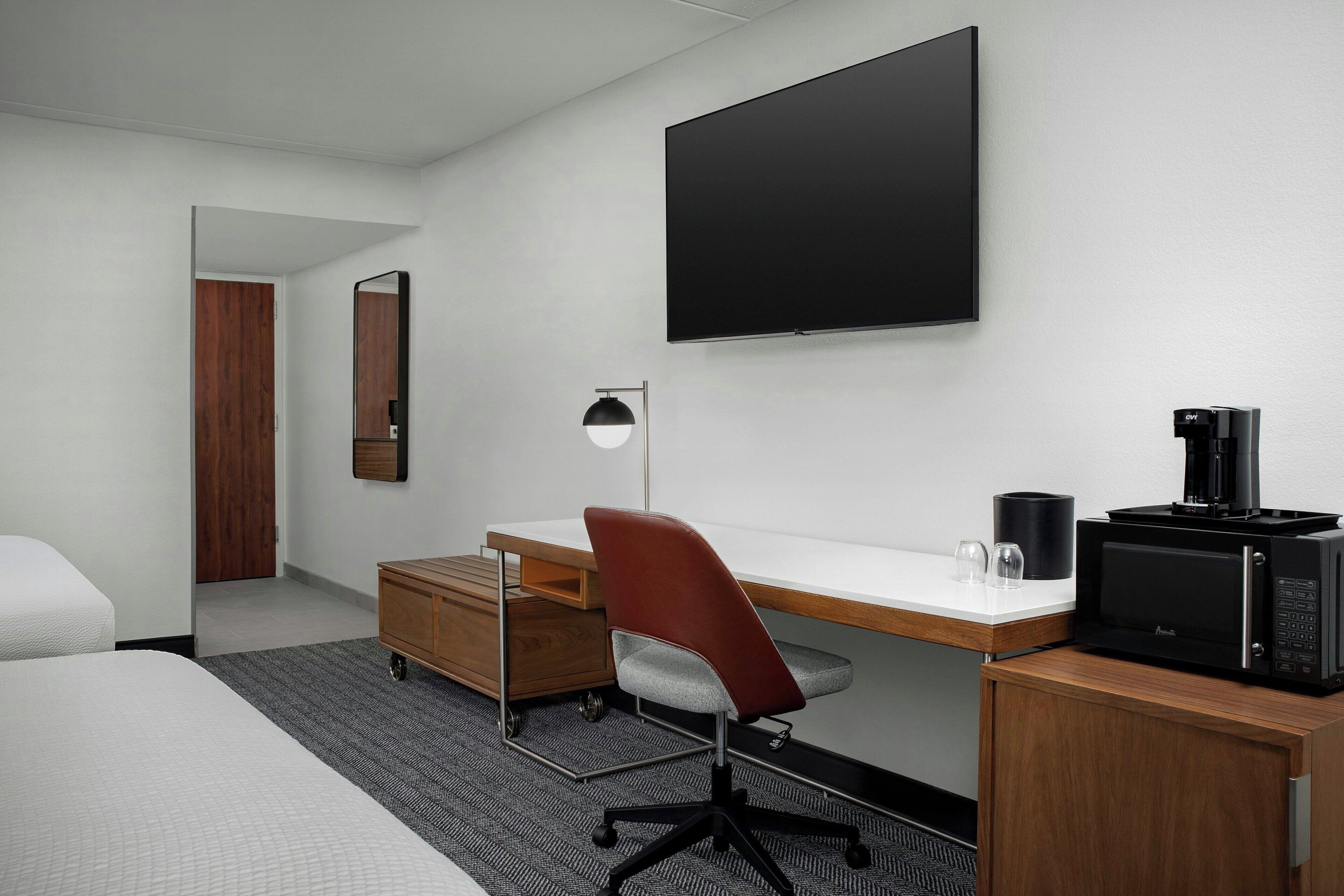 Habitación de hotel con cama, escritorio, silla, televisor de pantalla plana, cafetera y microondas.