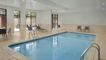 A swimming pool with lounge chairs and a sunbed area, surrounded by tiled walls and large windows.