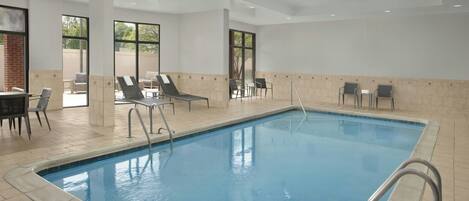 Une piscine entourée de chaises longues et d’un espace dédié au bronzage, le tout bordé de murs carrelés et doté de grandes fenêtres.