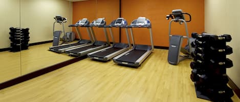 A gym with four treadmills, a weight stack, and a large mirror.