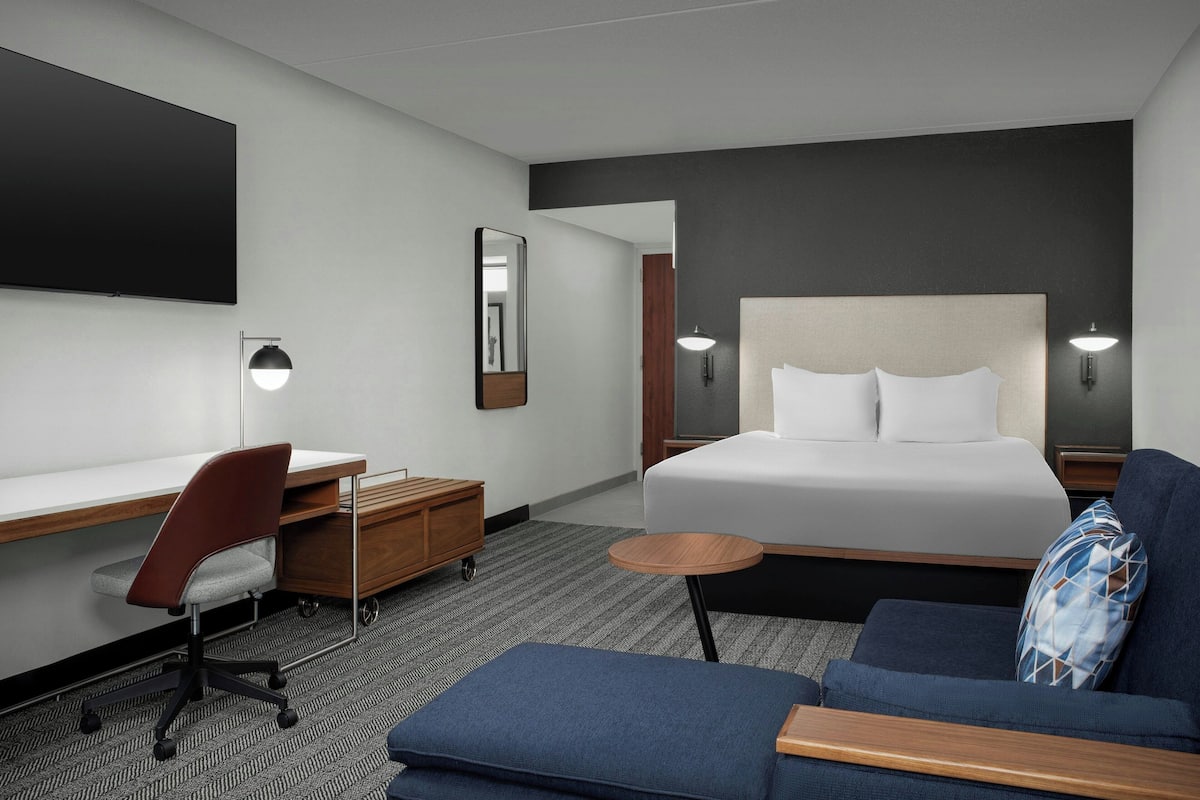 Une chambre d’hôtel avec un grand lit, un bureau avec une chaise, une petite table ronde et un canapé.