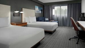 Habitación de hotel con dos camas, un escritorio, una silla, una lámpara y una ventana con cortinas.