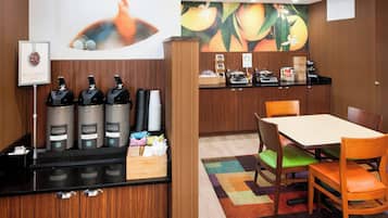 Una estación de café con tres dispensadores, una barra con una máquina de café y una mesa con sillas.