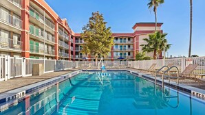 A swimming pool with a white fence, palm trees, and a multi-story building with balconies. - Days Inn by Wyndham York Alabama (York)