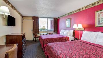 A hotel room with two beds, a desk, a chair, a TV, and a window with curtains.