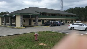 A motel with a covered parking area, a fire hydrant, and a tall communication tower in the background. - Days Inn by Wyndham York Alabama (York)