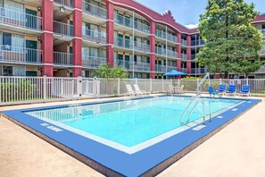 A rectangular pool with a blue edge, surrounded by a white fence. In the background, there is a multi-story building with balconies and a tree. - Days Inn by Wyndham York Alabama (York)