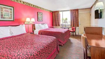 Una habitación de hotel con dos camas, un escritorio, una silla y un ventanal con cortinas.