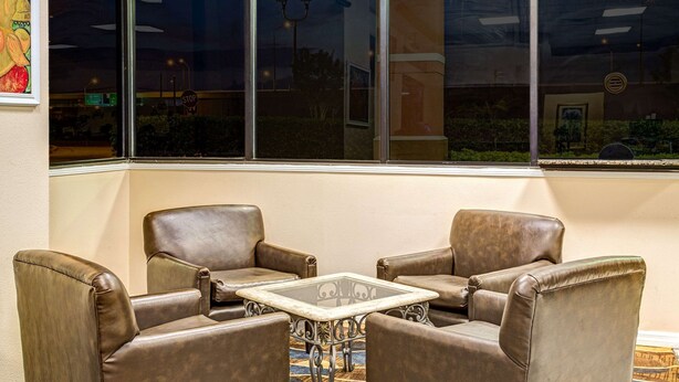 A corner seating area with four leather chairs and a glass-top table, positioned near a large window with a view of the outside. - Days Inn by Wyndham York Alabama (York)