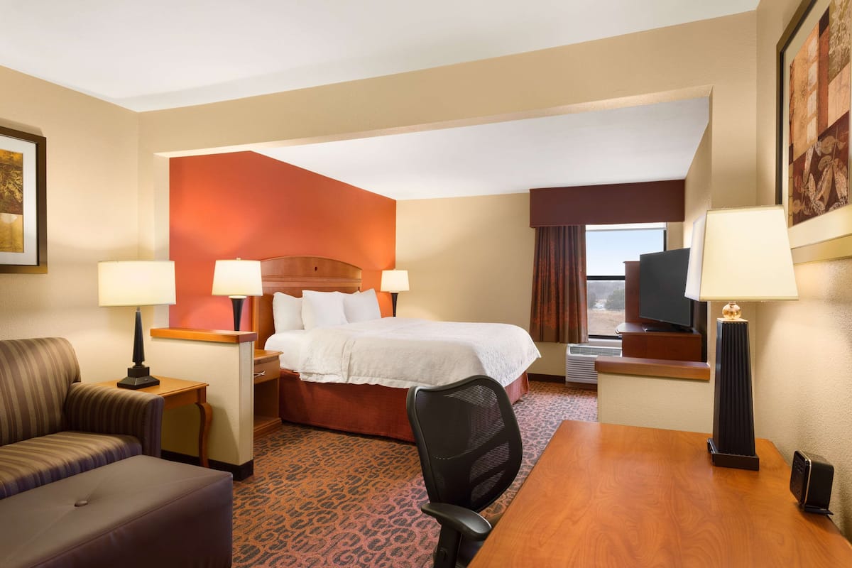 A hotel room with a bed, a desk, a chair, a TV, and two lamps.
